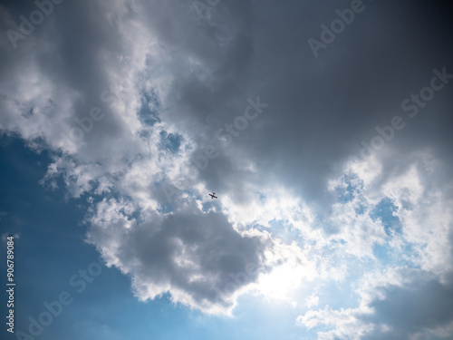 Obraz na płótnie Airplane flying high up in the sky below dark blue stormy clouds with sun shining through them. w salonie
