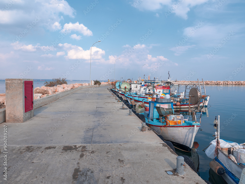 Various motor boats moored, tied up at the concrete pier in Mediterranean sea in Larnaca city, Cyprus. Rocky curved wave breaker, blue water and white clouds in the sky