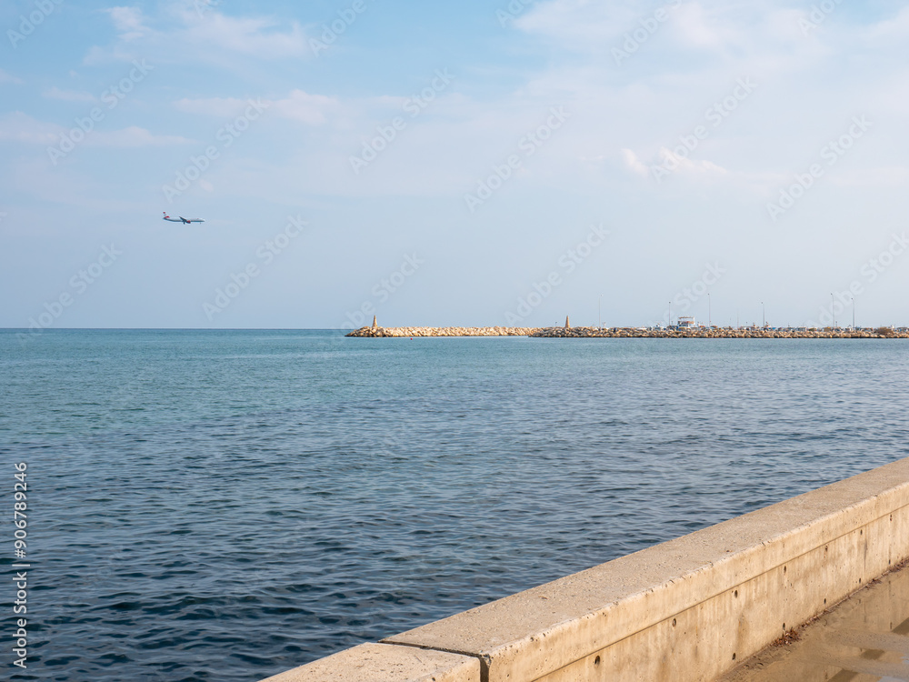Airplane preparing to land at the airport of Larnaca, Cyprus. Flying low above calm smooth blue Mediterranean sea with rocky wave breaker and promenade.
