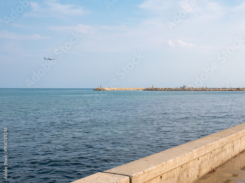 Obraz na płótnie Airplane preparing to land at the airport of Larnaca, Cyprus. Flying low above calm smooth blue Mediterranean sea with rocky wave breaker and promenade. w salonie