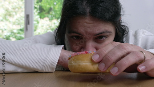 Obraz na płótnie A woman lying on a table, eyes fixed on a colorful sprinkled donut, conveying th