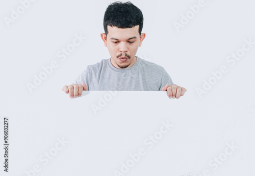 shocked expression of asian man looking down while holding banner blank signboard or copyspace for slogan