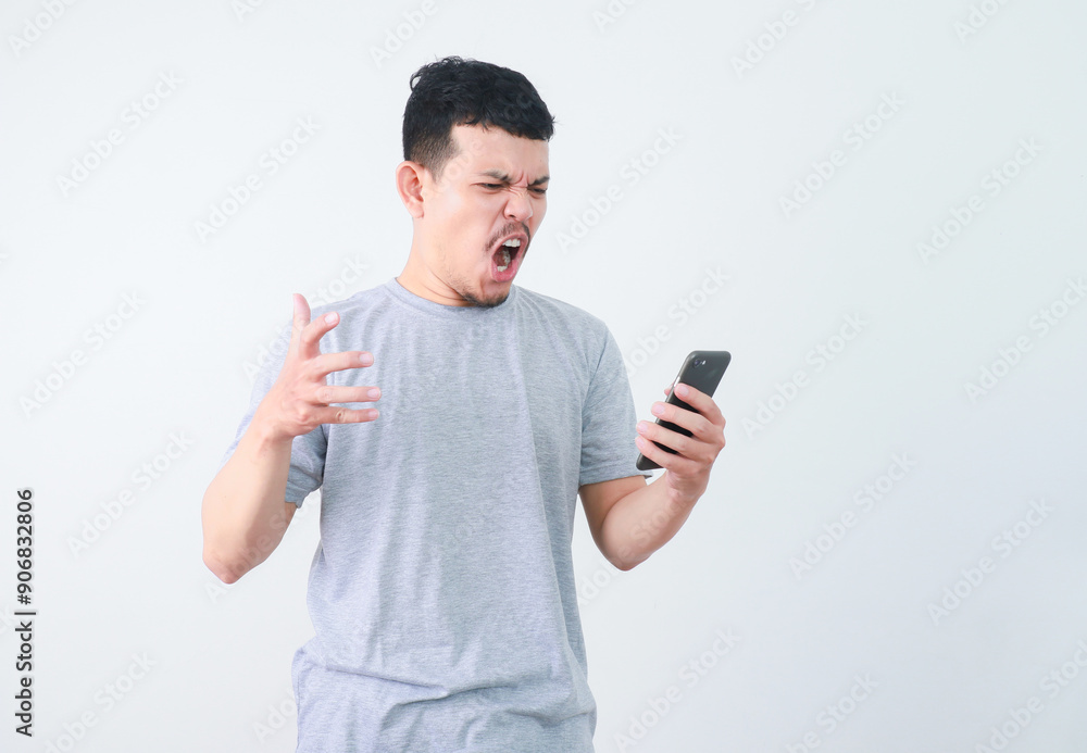 Angry Asian young man in grey t-shirt get mad on the smartphone. Angry Asian young man in grey t-shirt get mad on the smartphone.