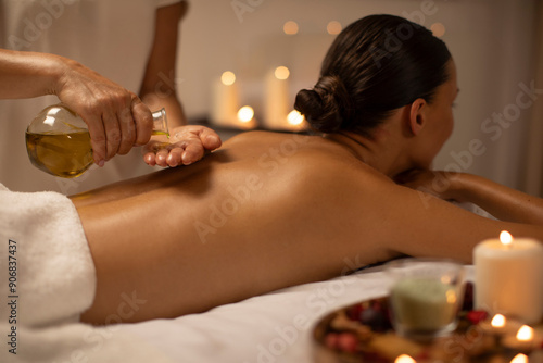 Massage therapist pouring oil on lady back at luxury spa decorated with candles, body care concept. Woman enjoying relaxing massage with aromatherapy photo