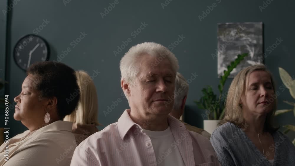 Arc shot of ethnically diverse senior people meditating with their eyes closed while sitting back to back in circle in modern group therapy class Arc shot of ethnically diverse senior people meditating with their eyes closed while sitting back to back in circle in modern group therapy class