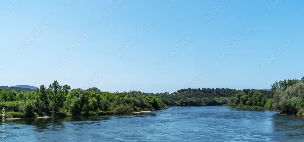 A tranquil river cuts through lush foliage under an expansive blue sky, with distant hills rolling into the horizon, embodying serene natural beauty. A tranquil river cuts through lush foliage under an expansive blue sky, with distant hills rolling into the horizon, embodying serene natural beauty.