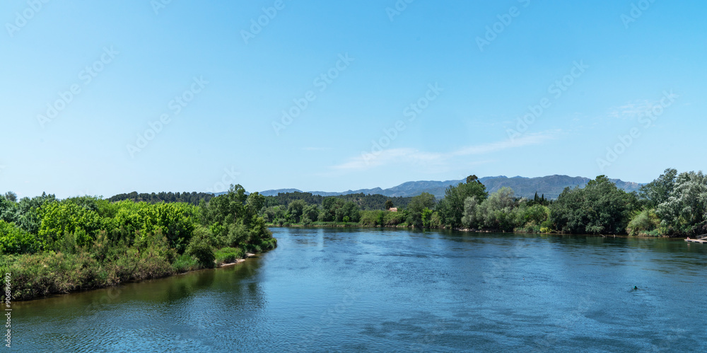 Overlooking a serene river, the foreground showcases a rustic terracotta-tiled roof, with lush greenery on the banks and distant mountains under a clear expansive sky. Overlooking a serene river, the foreground showcases a rustic terracotta-tiled roof, with lush greenery on the banks and distant mountains under a clear expansive sky.