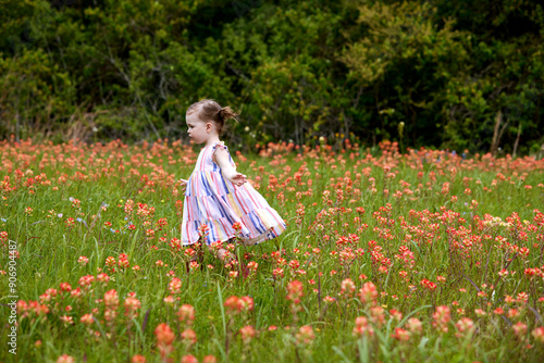 A little girl in a red, blue and yellow striped sundress, opens her arms to the wind as she crosses a field of orange wildflowers.
