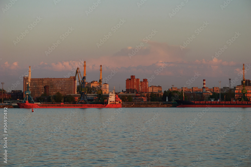 Industrial harbor at sunset, with cargo ships and cranes silhouetted against a calm waterfront cityscape. Industrial harbor at sunset, with cargo ships and cranes silhouetted against a calm waterfront cityscape.