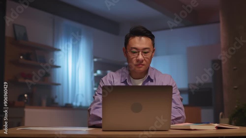 Serious asian businessman with glasses use laptop typing on keyboard and make notes. Working at night time. 360 degree. Camera moving around