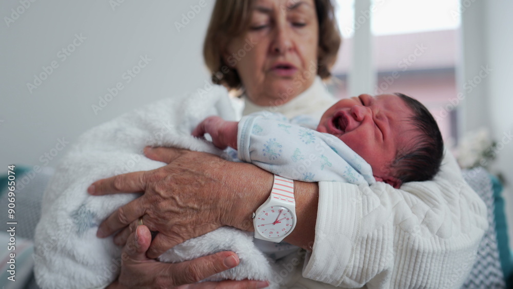Grandmother trying to comfort crying baby newborn craddling him in her arms standing home living-room. infant during first week of life Grandmother trying to comfort crying baby newborn craddling him in her arms standing home living-room. infant during first week of life