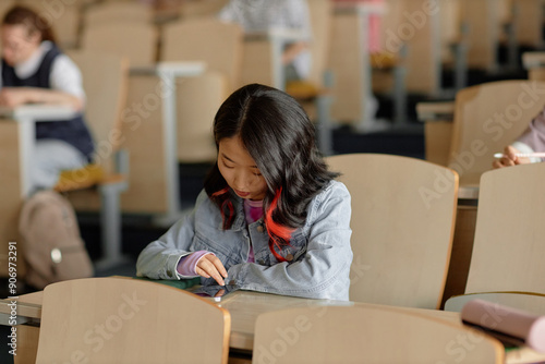 Fotografie Young Asian female student on phone checking social media and chatting during un
