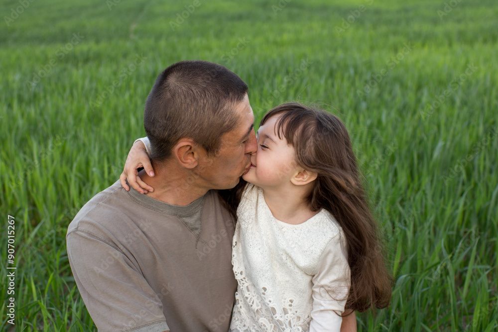 Obraz premium a little girl with long hair with her father in a field of green wheat. young wheat. father and daughter