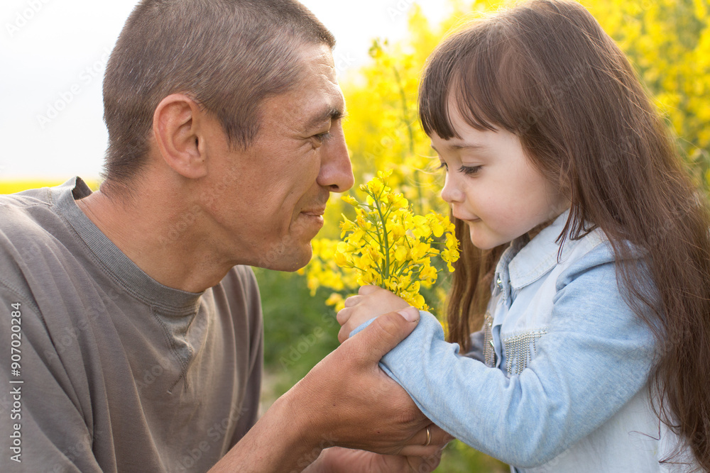 a little girl with her father in a field of flowering yellow field. father holding daughter's hands a little girl with her father in a field of flowering yellow field. father holding daughter's hands