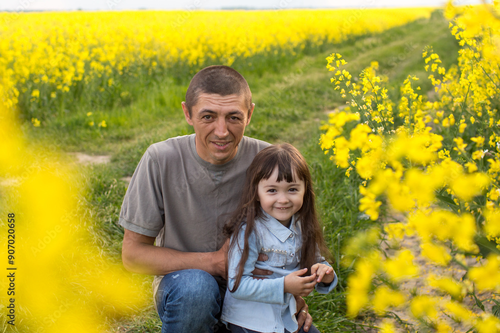 a little girl with her father in a field of flowering yellow field. father holding daughter's hands a little girl with her father in a field of flowering yellow field. father holding daughter's hands