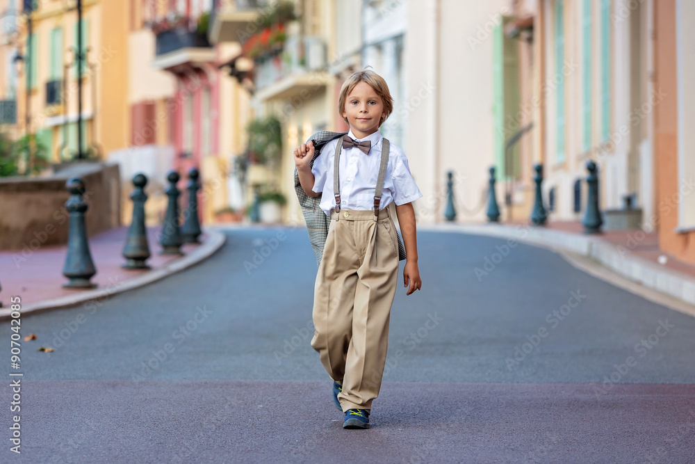 Smart casual children in suits, ties and bows, walking on a narrow street with houses in Monaco-Ville, Monaco. Business clothing, teenagers, preschool boy and mother Smart casual children in suits, ties and bows, walking on a narrow street with houses in Monaco-Ville, Monaco. Business clothing, teenagers, preschool boy and mother