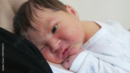 Newborn baby infant close-up face during first week of life, adorbale little newborn resting on mother's arms photo