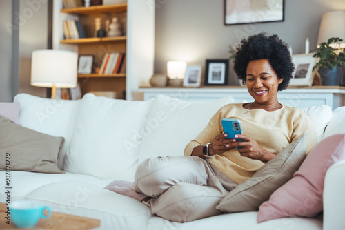 Cropped shot of an attractive young woman using her cellphone in the living room during the day. Female Using Smartphone in Stylish Living Room. Young Woman at Home photo