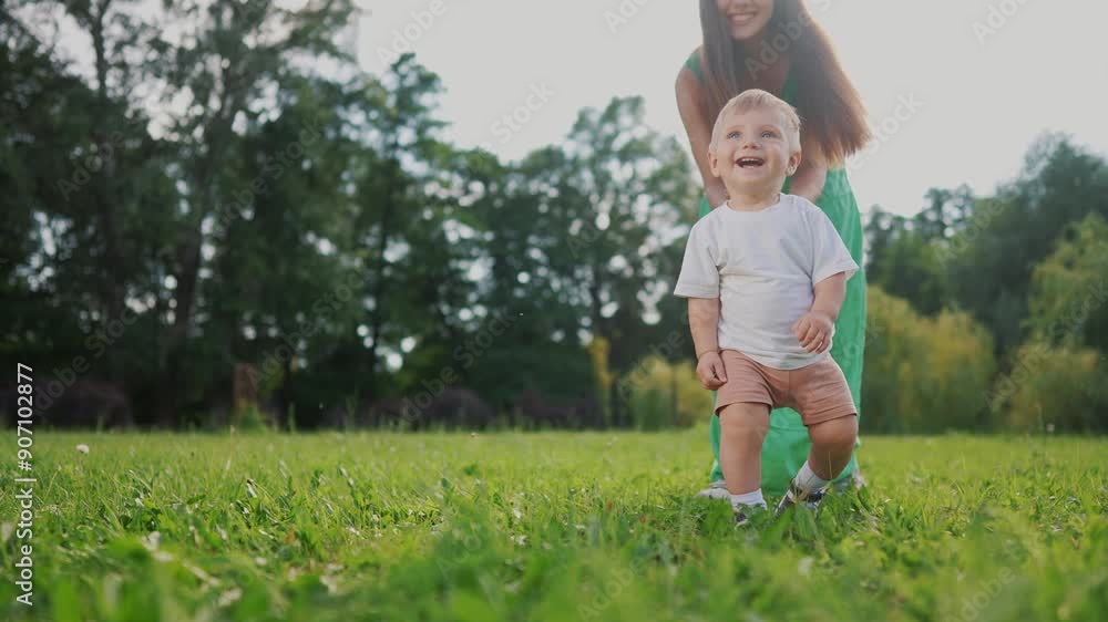 Mom and baby taking the first steps. Happy family kid dream concept. A baby is walking on the grass in a park. Mom and baby walking on grass on first steps lifestyle in the park.