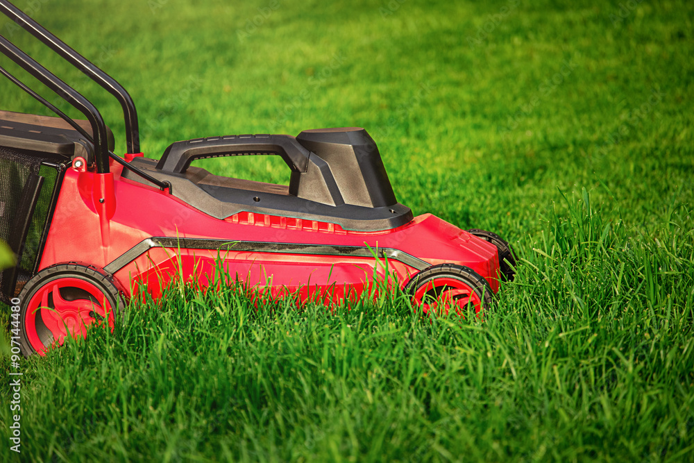 A red and black lawnmower on a background of green grass. A red and black lawnmower on a background of green grass.