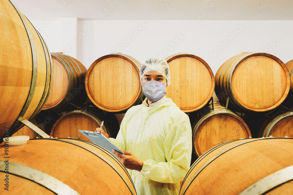 Male employees wearing coats and masks inspect the oak wine cellar taking notes and reporting neatness oak barrel temperature controlled room maintain quality and taste within production facilities. Male employees wearing coats and masks inspect the oak wine cellar taking notes and reporting neatness oak barrel temperature controlled room maintain quality and taste within production facilities.