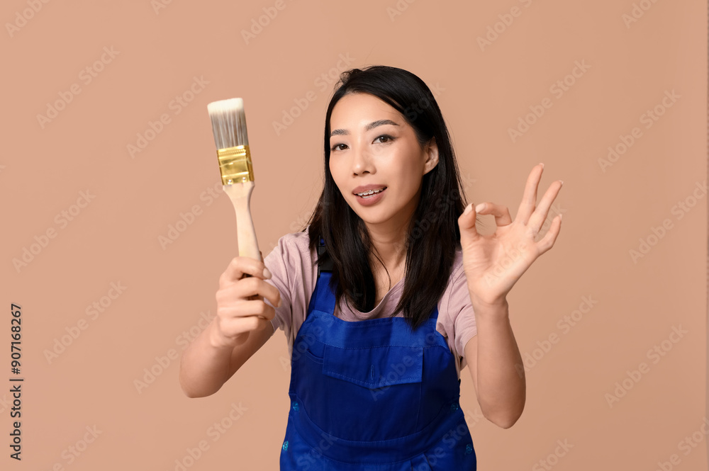 Female Asian happy painter with brush showing OK gesture on brown background Female Asian happy painter with brush showing OK gesture on brown background