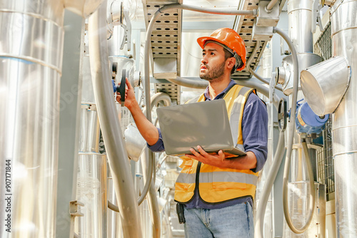 Photography Male HAVC refrigeration system technician stands holding laptop recording preventative inspection refrigeration equipment refrigerant level control valve into the system and checking leaks at various
