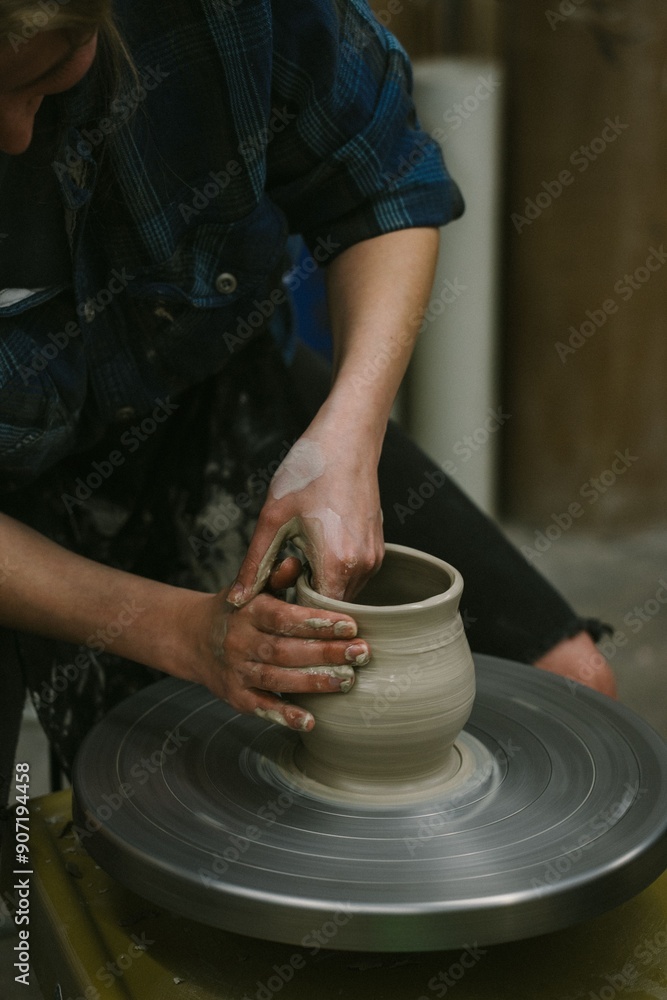 Person shapes pottery on a spinning wheel in a workshop, focusing on the hands and clay. Person shapes pottery on a spinning wheel in a workshop, focusing on the hands and clay.