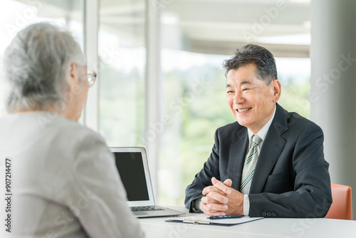シニア女性を接客・カウンセリング・面談するスーツ姿のアジア人シニア男性ビジネスマン 