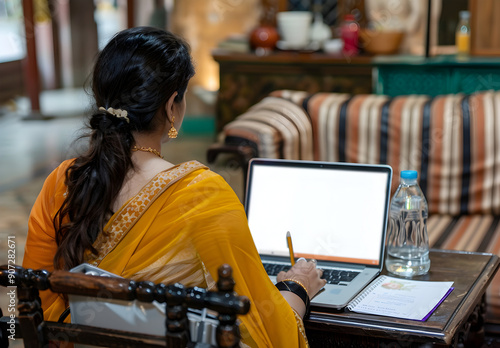 Woman in a yellow saree working on a laptop.