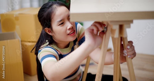 Handheld high angle view shot, Young Asian woman sitting on the floor and assembling wooden furniture in a new house. Moving house and lifestyle concept.