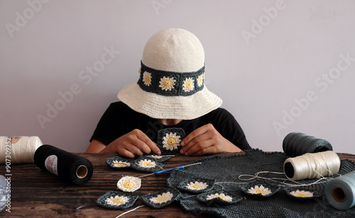 Woman wear daisy motifs crohet hat, surrounded by an array of colorful supplies materials for diy project, leisure with creativity handmade in workspace