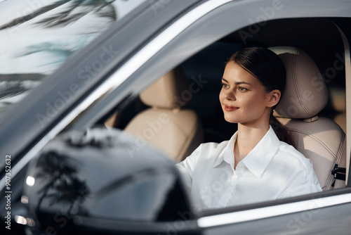 A cheerful woman sits in the driver's seat of a car, her hand on the steering wheel and a bright smile on her face, exuding confidence and happiness while preparing to drive