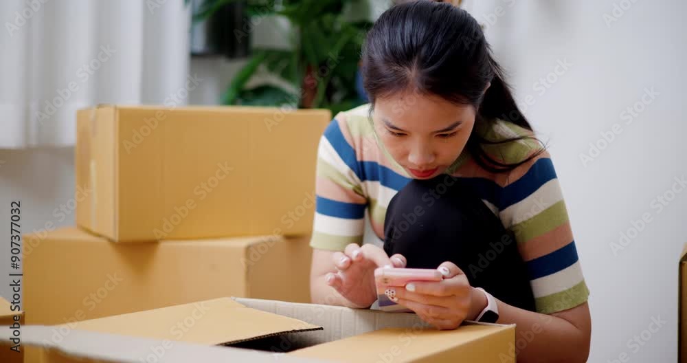 Handheld selective focus shot, Young asian woman sitting on the floor searching for home decorating ideas on her mobile phone in her new house. Moving and lifestyle concepts. Handheld selective focus shot, Young asian woman sitting on the floor searching for home decorating ideas on her mobile phone in her new house. Moving and lifestyle concepts.