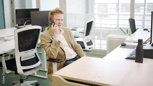 In a contemporary office setting, an individual wearing a blazer is engaged in a phone call while utilizing computers in a teamoriented environment, highlighting collaboration and effectiveness photo