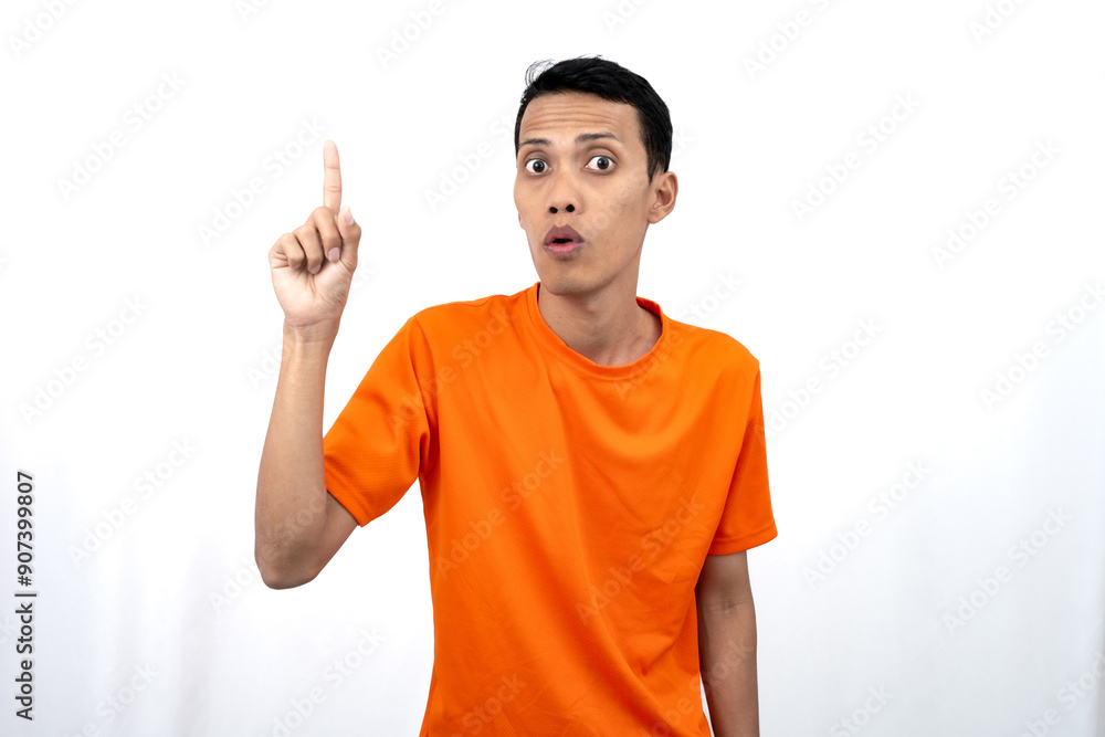 Portrait of a young Asian man wearing an orange t-shirt pointing upwards at copy space for promotional space. isolated on white background. Portrait of a young Asian man wearing an orange t-shirt pointing upwards at copy space for promotional space. isolated on white background.