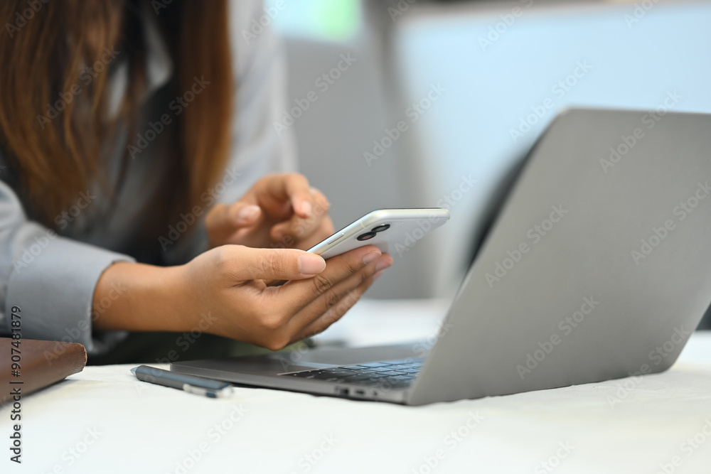 Young woman using mobile phone and working with laptop in living room Young woman using mobile phone and working with laptop in living room