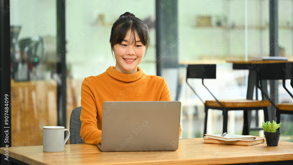 Pretty young Asian woman in yellow sweater using laptop in the cafe Pretty young Asian woman in yellow sweater using laptop in the cafe