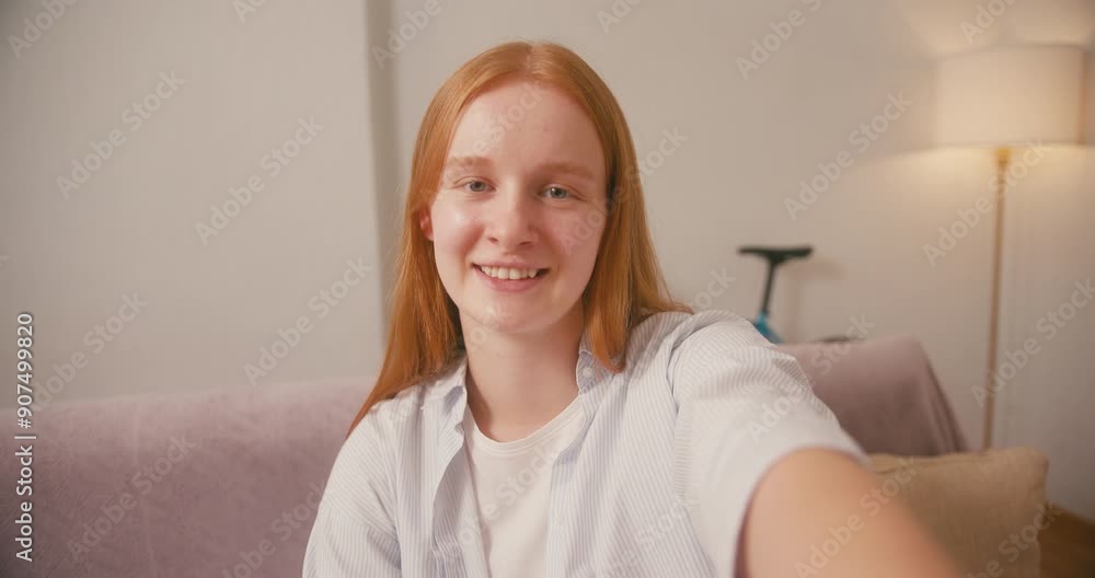 Red-haired woman waves hand in warm welcome on smartphone camera Red-haired woman waves hand in warm welcome on smartphone camera