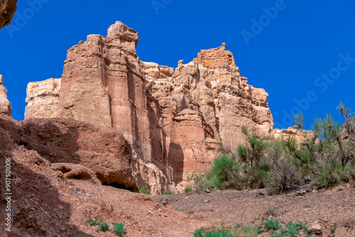 Great Charyn Canyon, Almaty, Kazakhstan. Valley of Castles. Bright blue sky with white clouds over a large lonely rock in the desert on a hot, sunny day with sparse vegetation. Without people