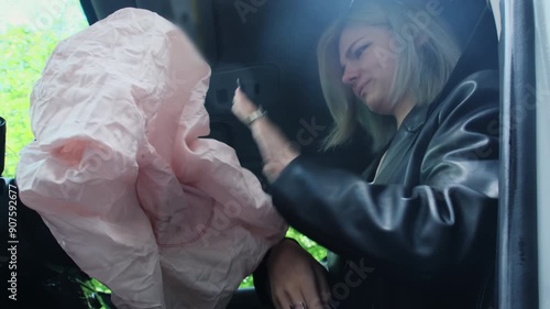 Airbag expands following vehicle accident. Angry young woman attempts to remove safety cushion opened towards face saving life of driver photo