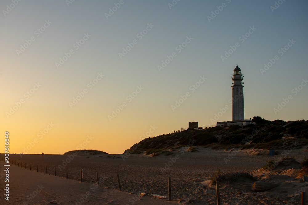 Obraz premium sunset over the trafalgar dunes crowned by the imposing mozarabic lighthouse of trafalgar.