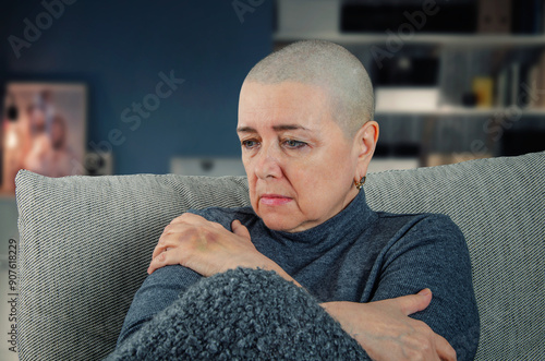 The image shows a woman with a shaved head, indicative of cancer treatment, sitting alone and seemingly lost in thought. The setting and her expression suggest a deep sense of loss and despair.