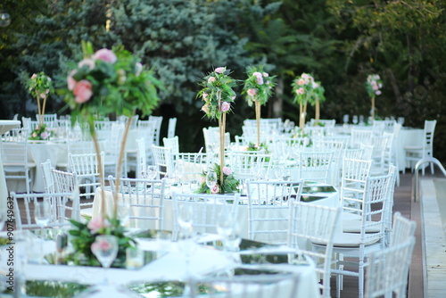 A beautiful outdoor wedding reception with white tables, gold accents, and lush greenery. The tables are set with elegant glassware and silverware, creating a romantic and intimate atmosphere