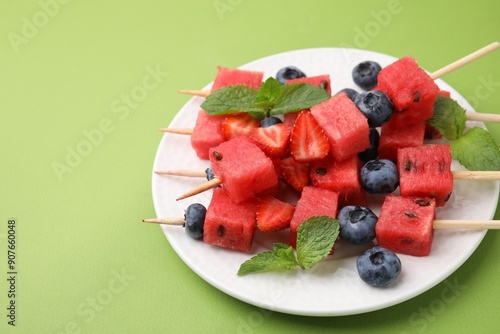 Skewers with tasty watermelon, strawberries, blueberries and mint on green table, closeup