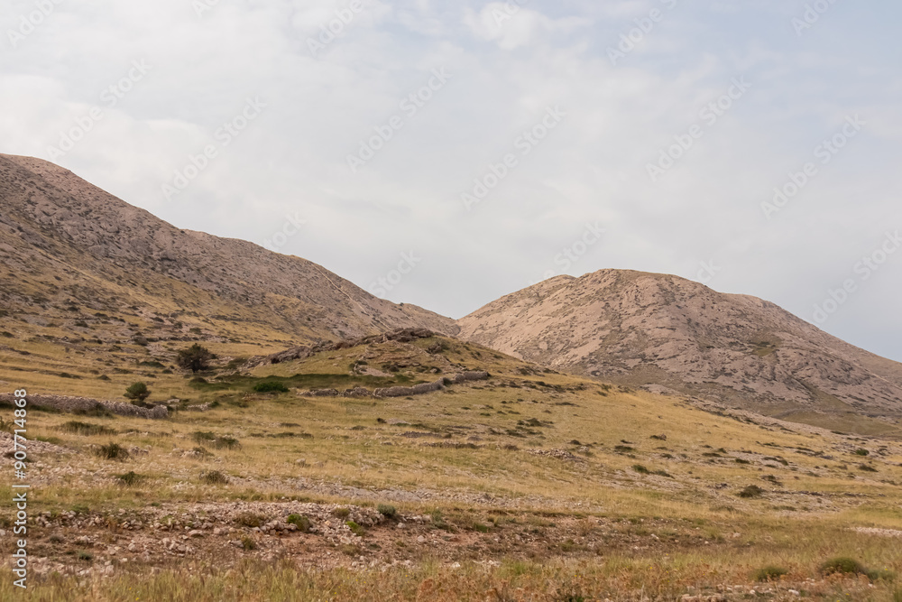 Panoramic view of rolling hills and rugged mountains peaks covered in patchwork of golden grasslands and sparse vegetation in Vela Luka bay on island Otok Krk, Primorje-Gorski Kotar, Croatia. Hiking Panoramic view of rolling hills and rugged mountains peaks covered in patchwork of golden grasslands and sparse vegetation in Vela Luka bay on island Otok Krk, Primorje-Gorski Kotar, Croatia. Hiking