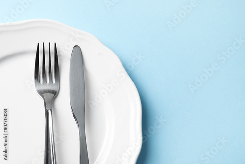 Stylish silver cutlery and plate on light blue background, top view. Space for text