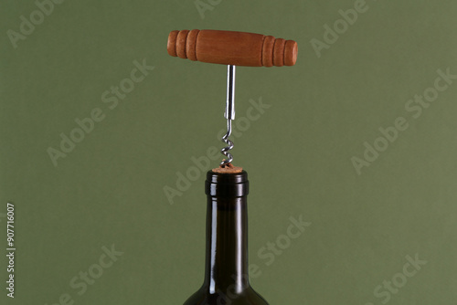 Wine bottle with corkscrew on olive background, closeup