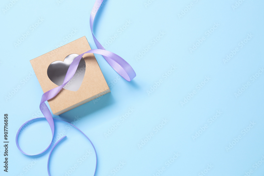 Beautiful violet ribbon and gift box with heart on light blue background, flat lay. Space for text Beautiful violet ribbon and gift box with heart on light blue background, flat lay. Space for text