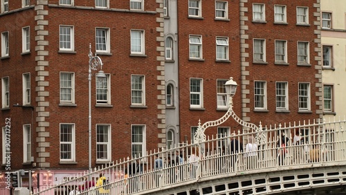 Valokuva People crossing the Ha'penny Bridge in Dublin with impressive Georgian Buildings